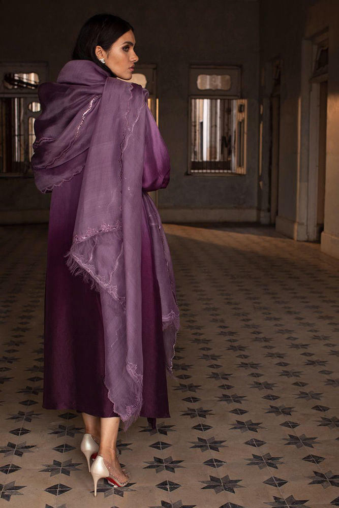 Woman in a long, dark purple dress with a matching shawl standing in a room with patterned carpet.