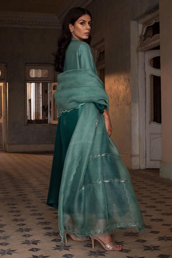 Woman in a teal traditional outfit standing in an indoor setting with patterned floor.
