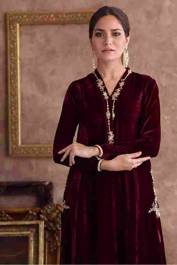 Woman wearing a burgundy velvet dress with gold embroidery in a decorative setting.