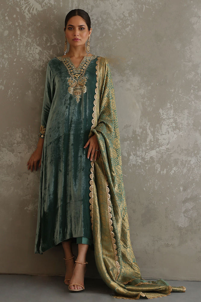 Woman wearing a traditional outfit with a green dress and gold dupatta against a gray background