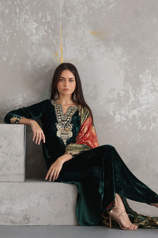 Woman in an elegant green dress with intricate patterns sitting on a concrete surface.