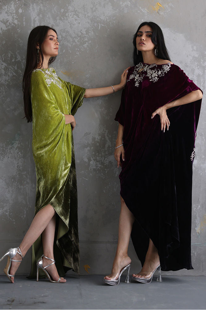 Two women wearing green and black sarees against a gray background