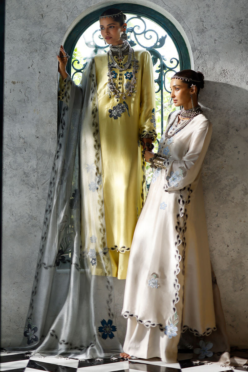 Two women in elegant dresses standing in a decorative archway.