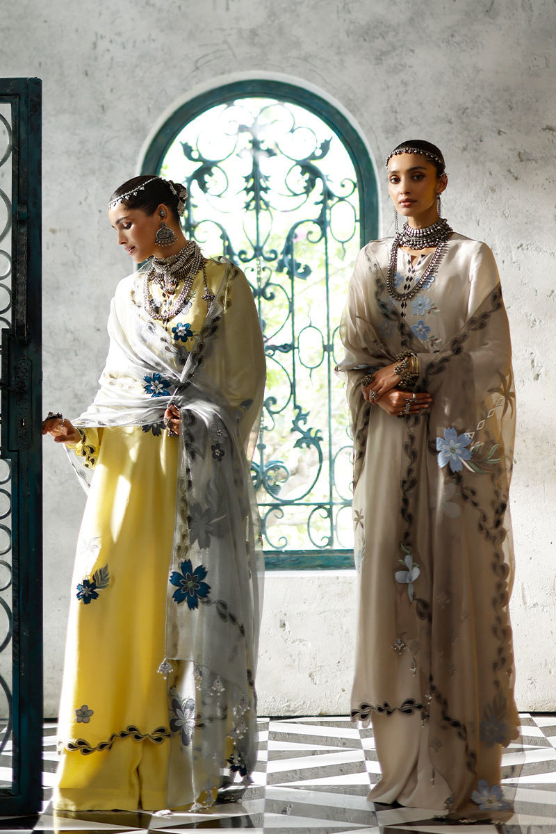 Two women in elegant outfits standing in a room with decorative archway.