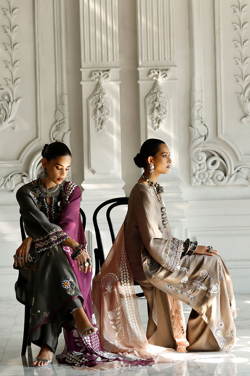 Two women in elegant outfits sitting in a room with ornate white walls.