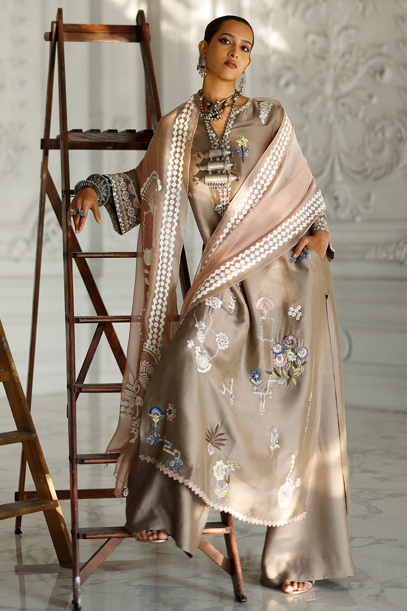 Woman in an embroidered saree standing next to a wooden ladder in a well-lit room.