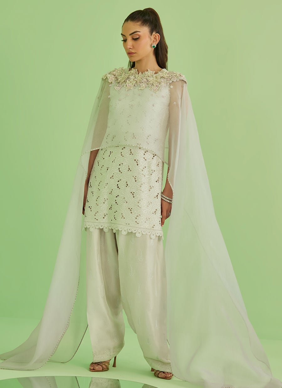 Woman wearing a light green traditional outfit with a cape against a green background