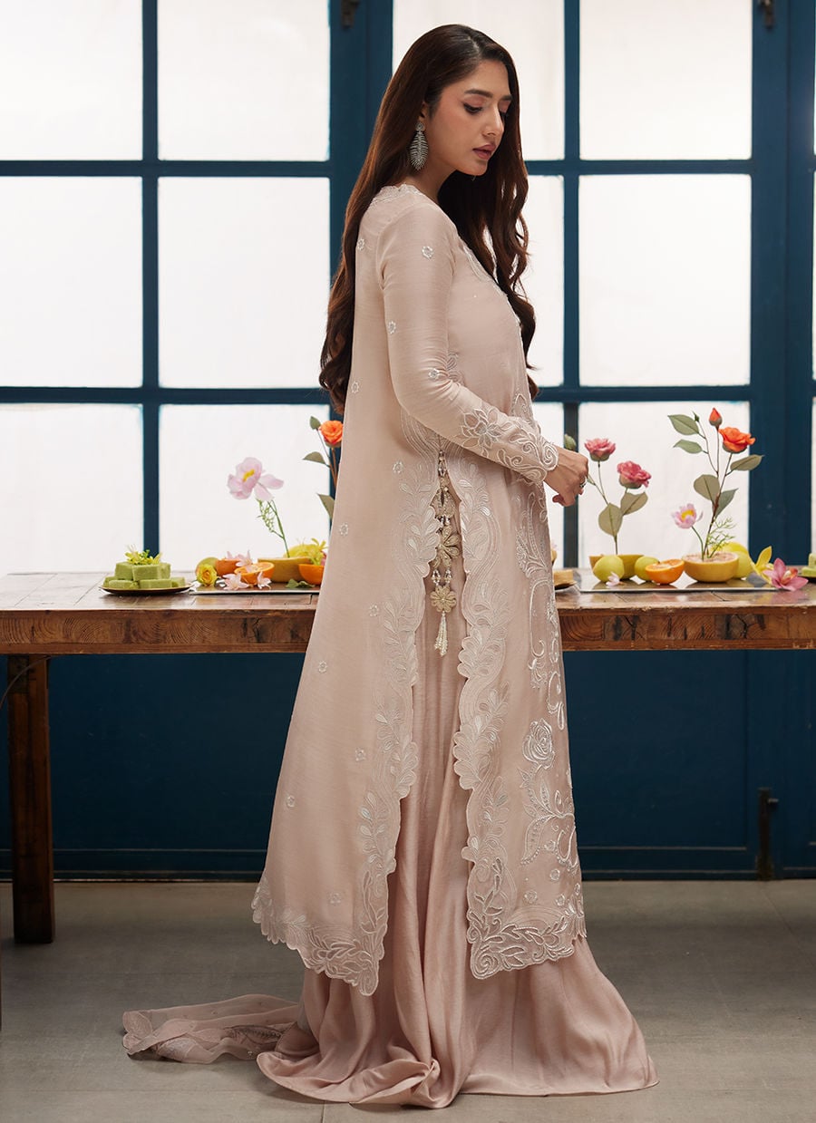 Woman in a light pink traditional outfit standing in a room with a table and decorative elements.