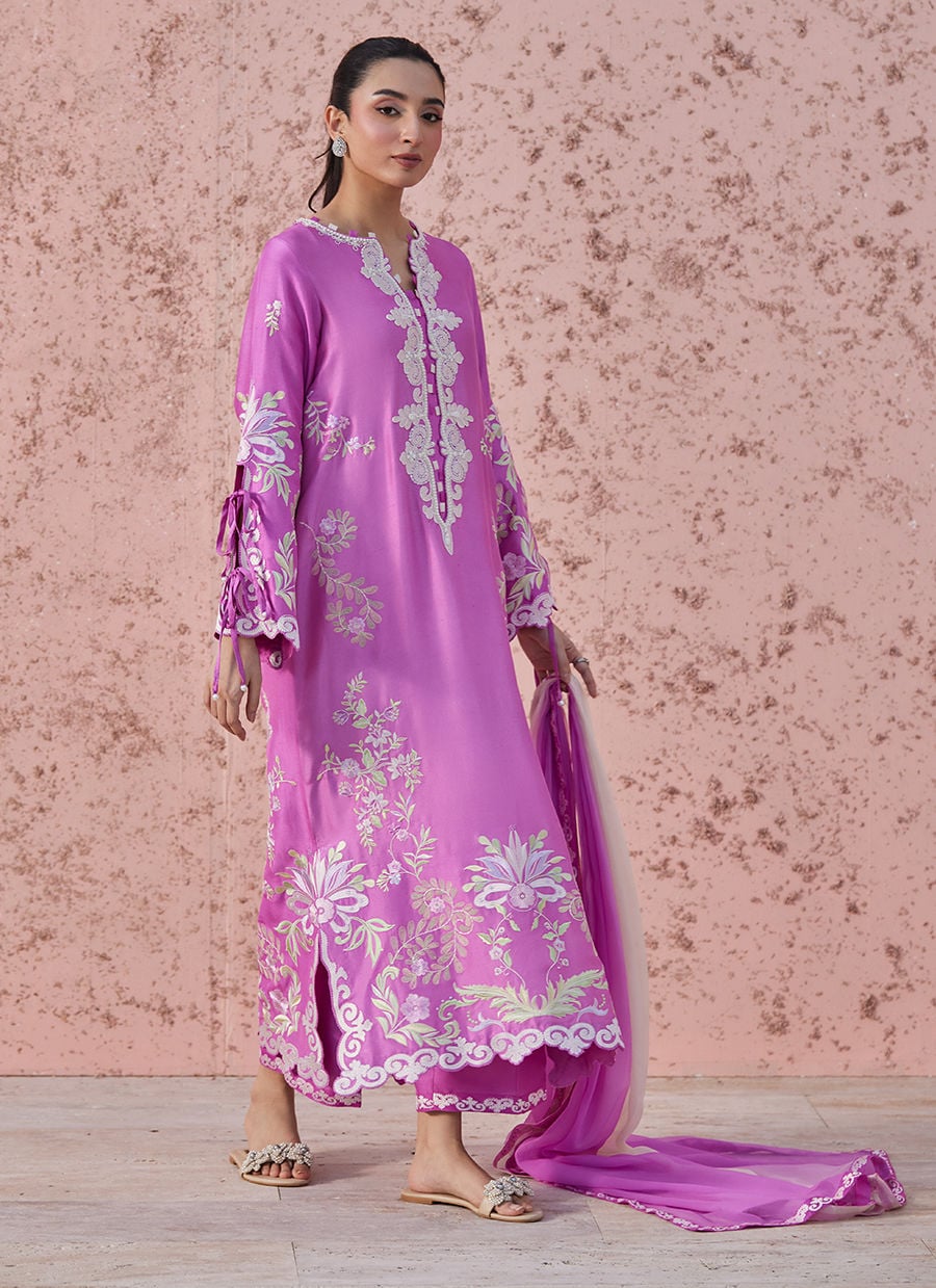 Woman wearing a pink embroidered outfit against a pink floral background