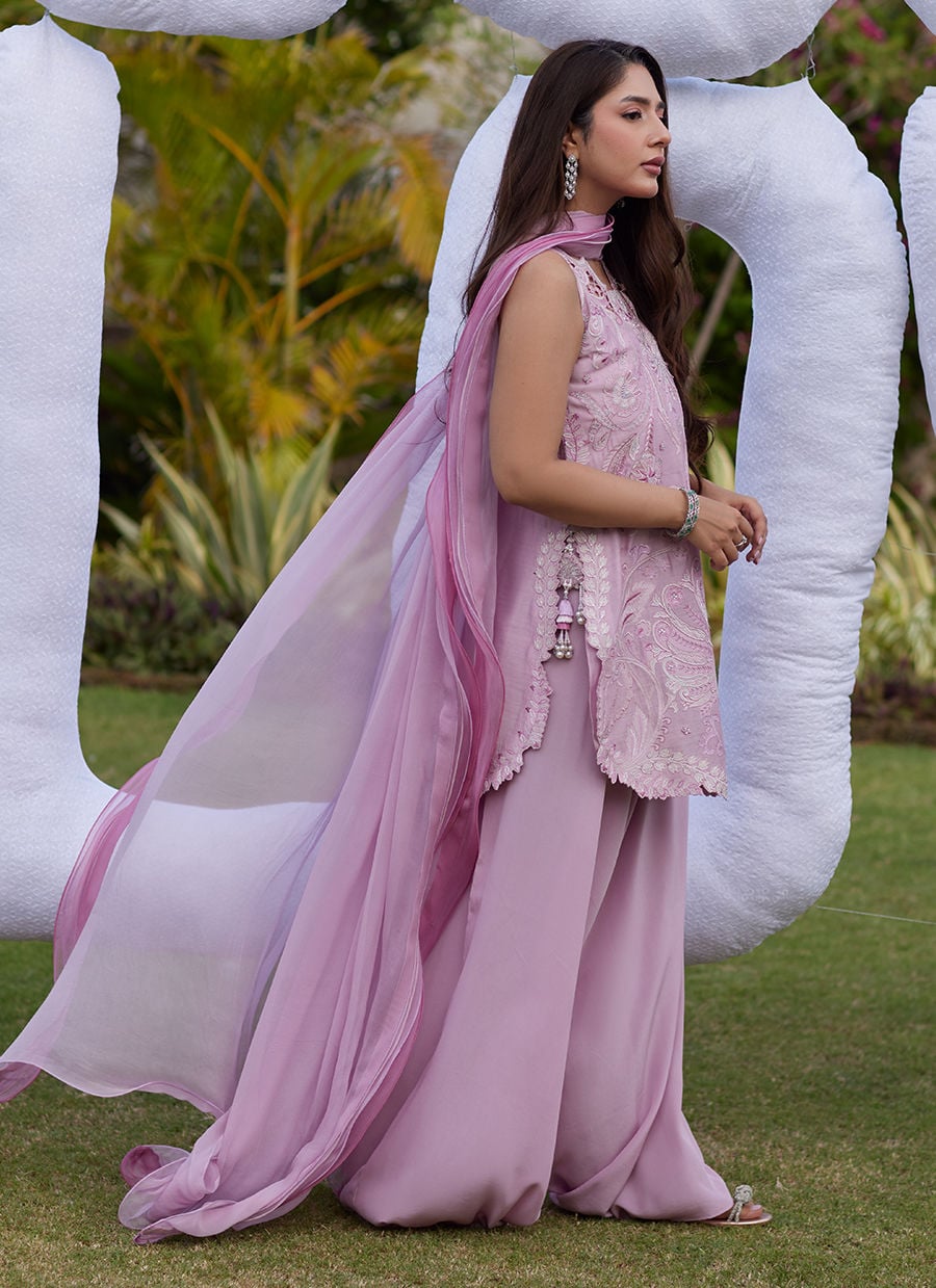 Woman in a pink traditional outfit standing outdoors with large white sculptures in the background.