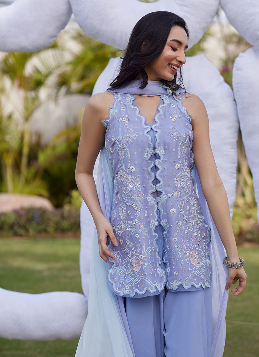 Woman in a light blue embroidered outfit standing outdoors with decorative elements in the background