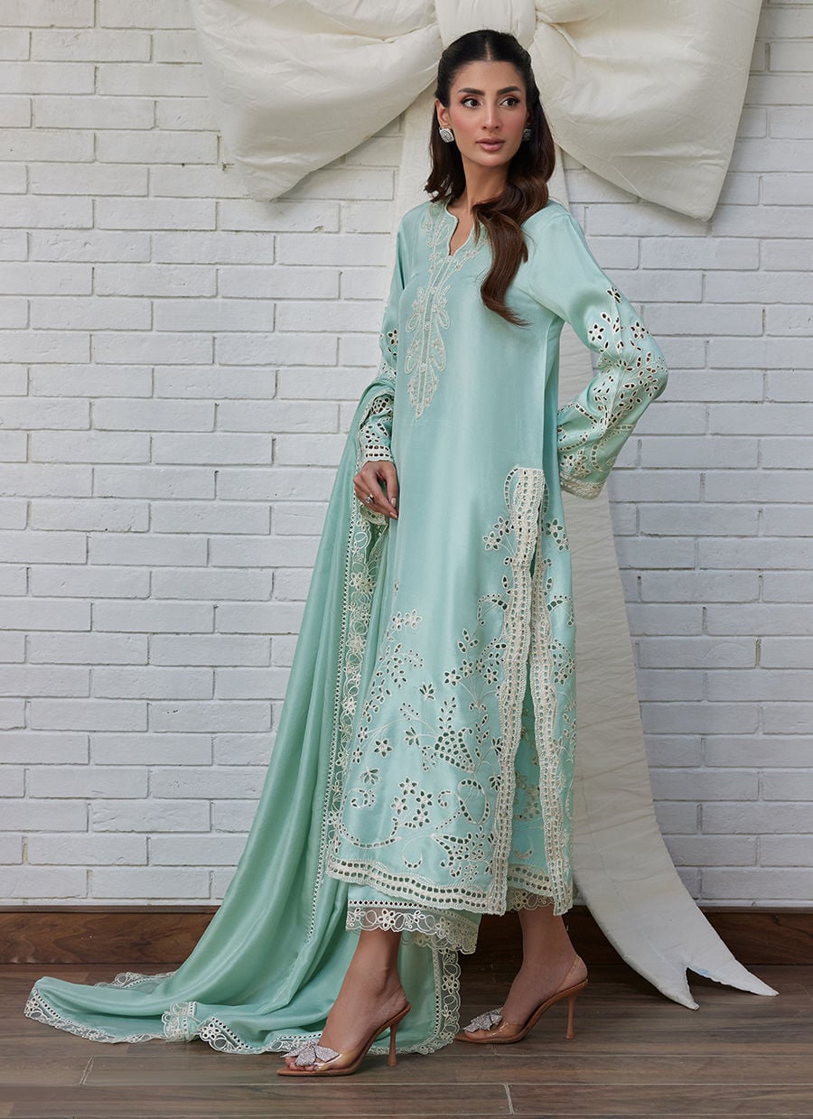 Woman wearing a light blue embroidered dress against a white brick wall with stylish pose.