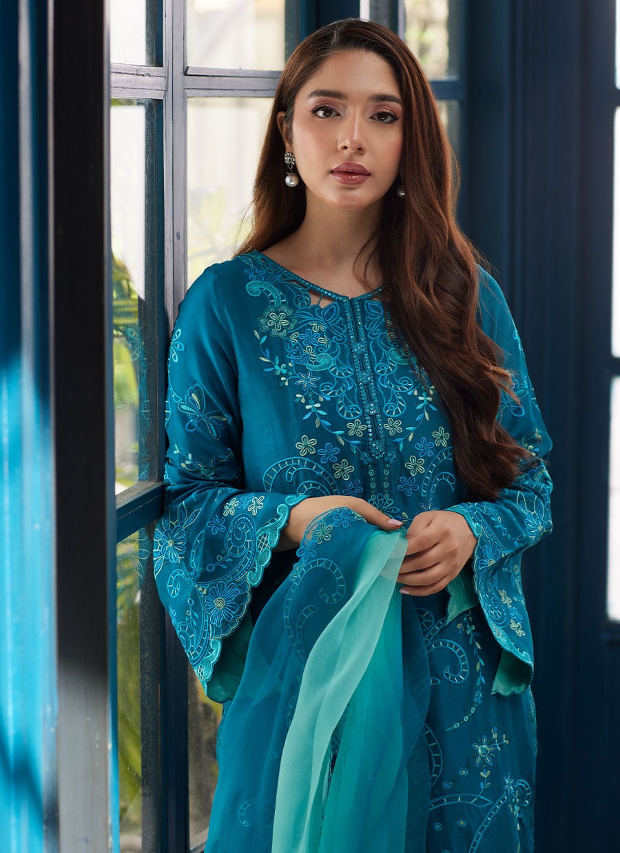 Woman in a teal embroidered outfit standing in a room.