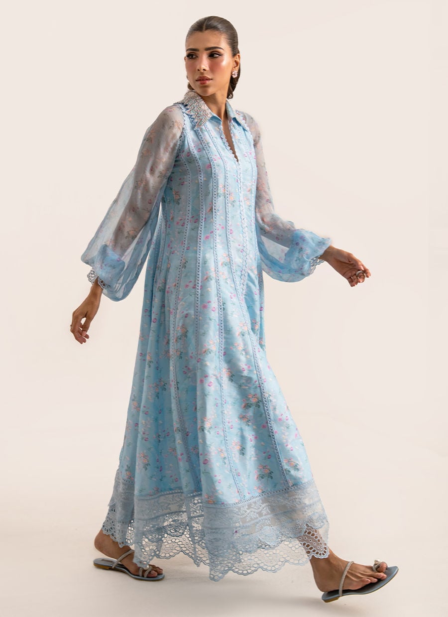 Woman wearing a light blue floral dress with sheer sleeves on a plain background