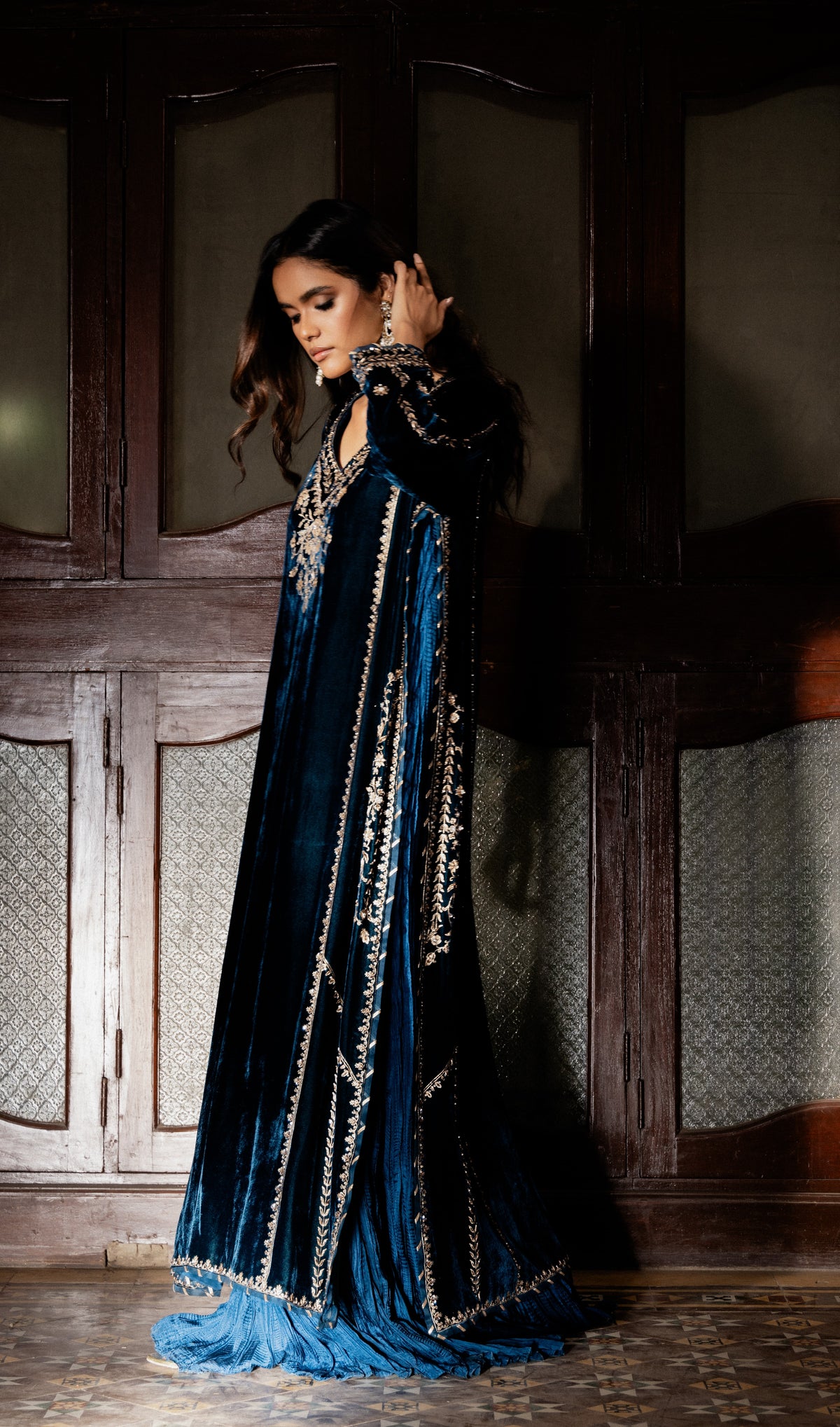 Woman wearing a blue velvet dress with intricate detailing in a dimly lit room.