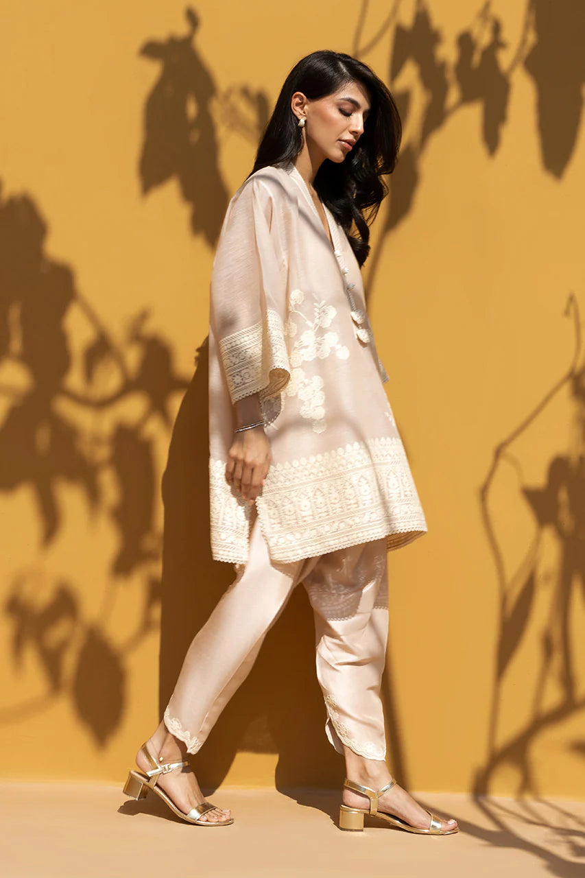 Woman in a light pink traditional outfit against a yellow wall with shadow patterns.