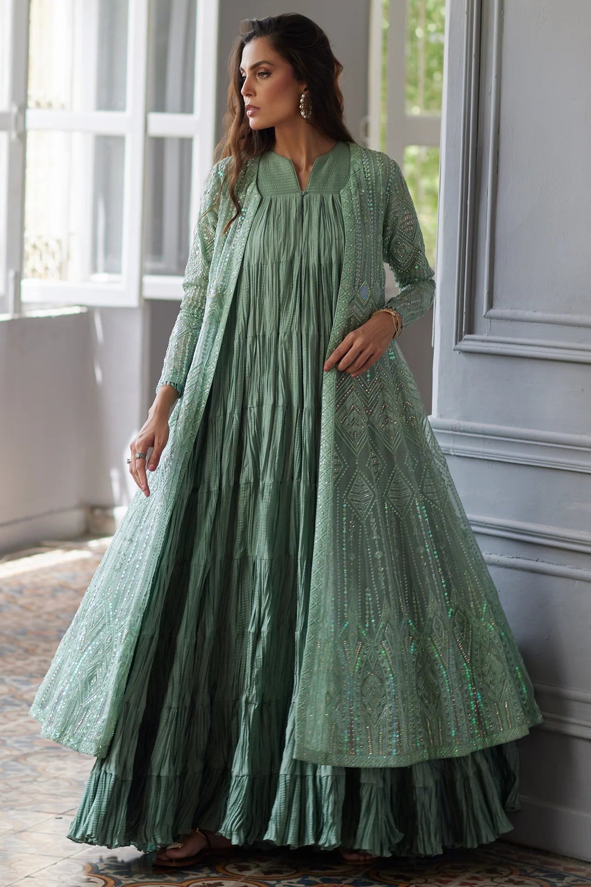Woman wearing a green traditional outfit standing in a room with large windows.