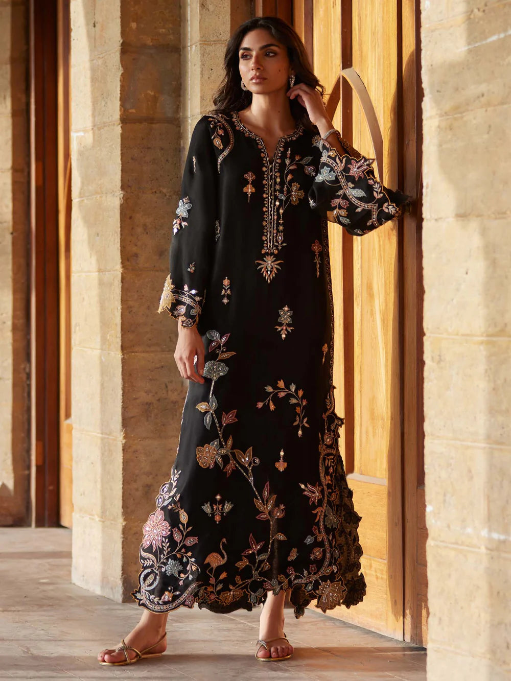 Woman wearing a black embroidered dress standing in front of a stone wall.