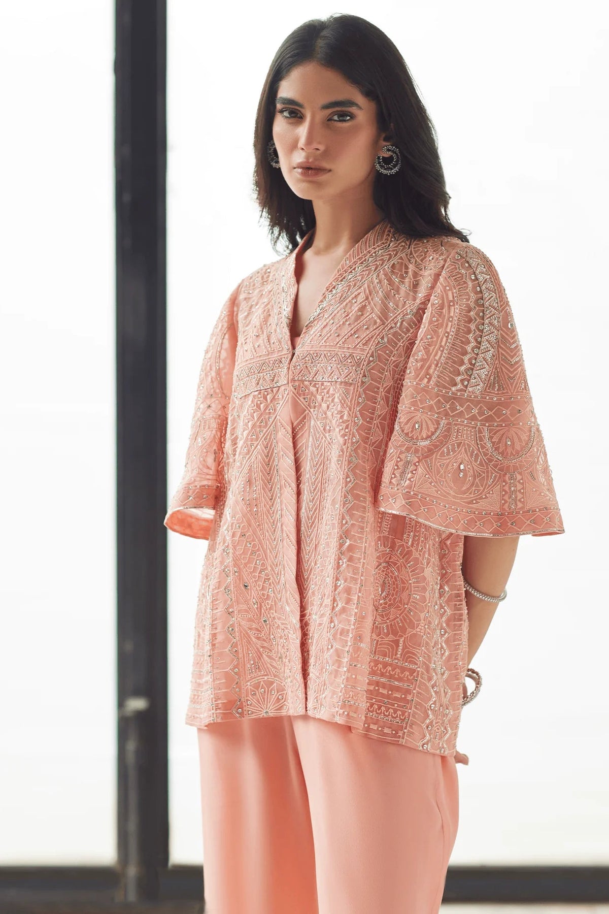 Woman wearing a pink embroidered top and pants in a minimal indoor setting