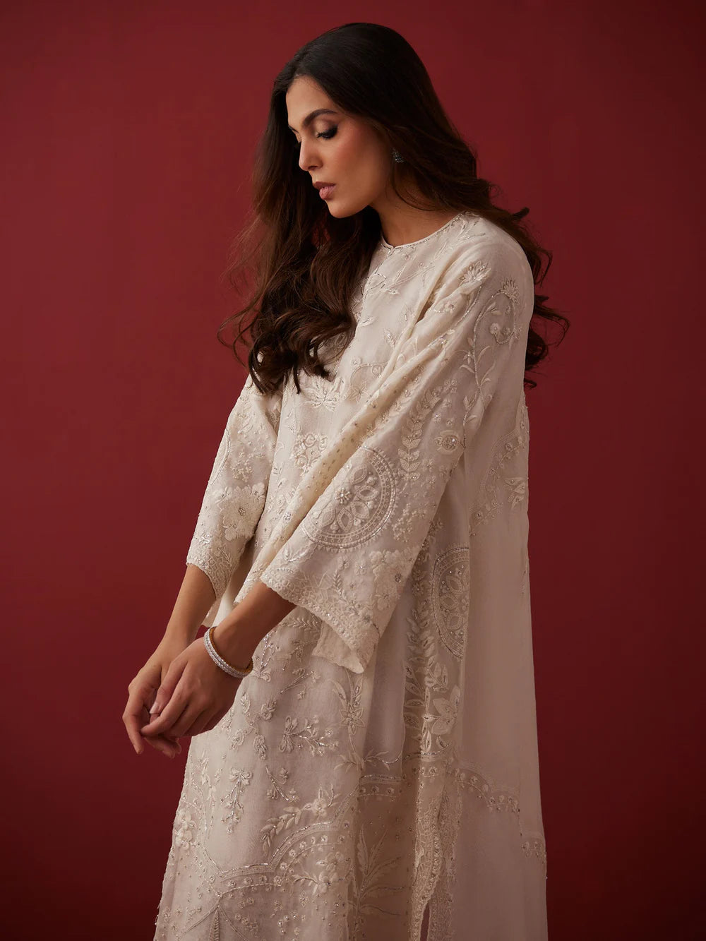 Woman wearing a white embroidered dress against a red background