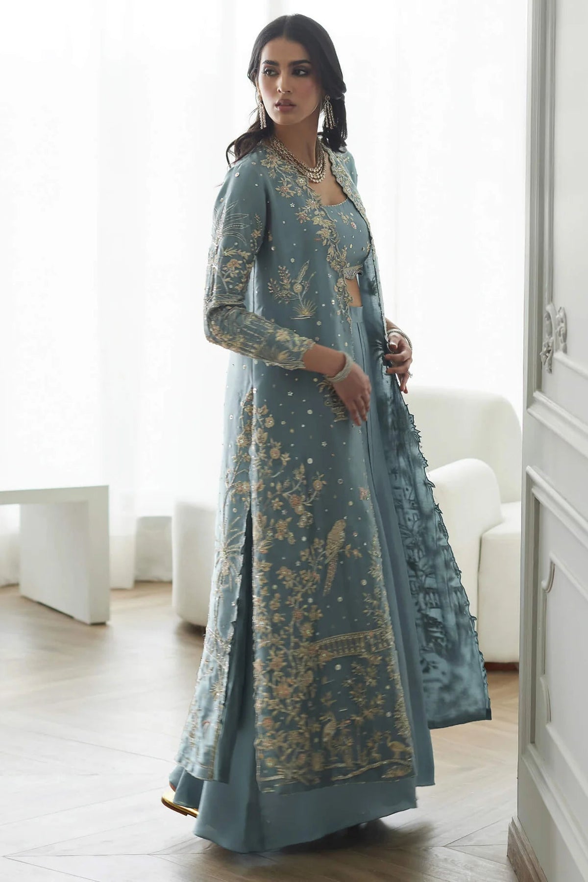Woman in a long, light blue embroidered dress standing in a bright room.