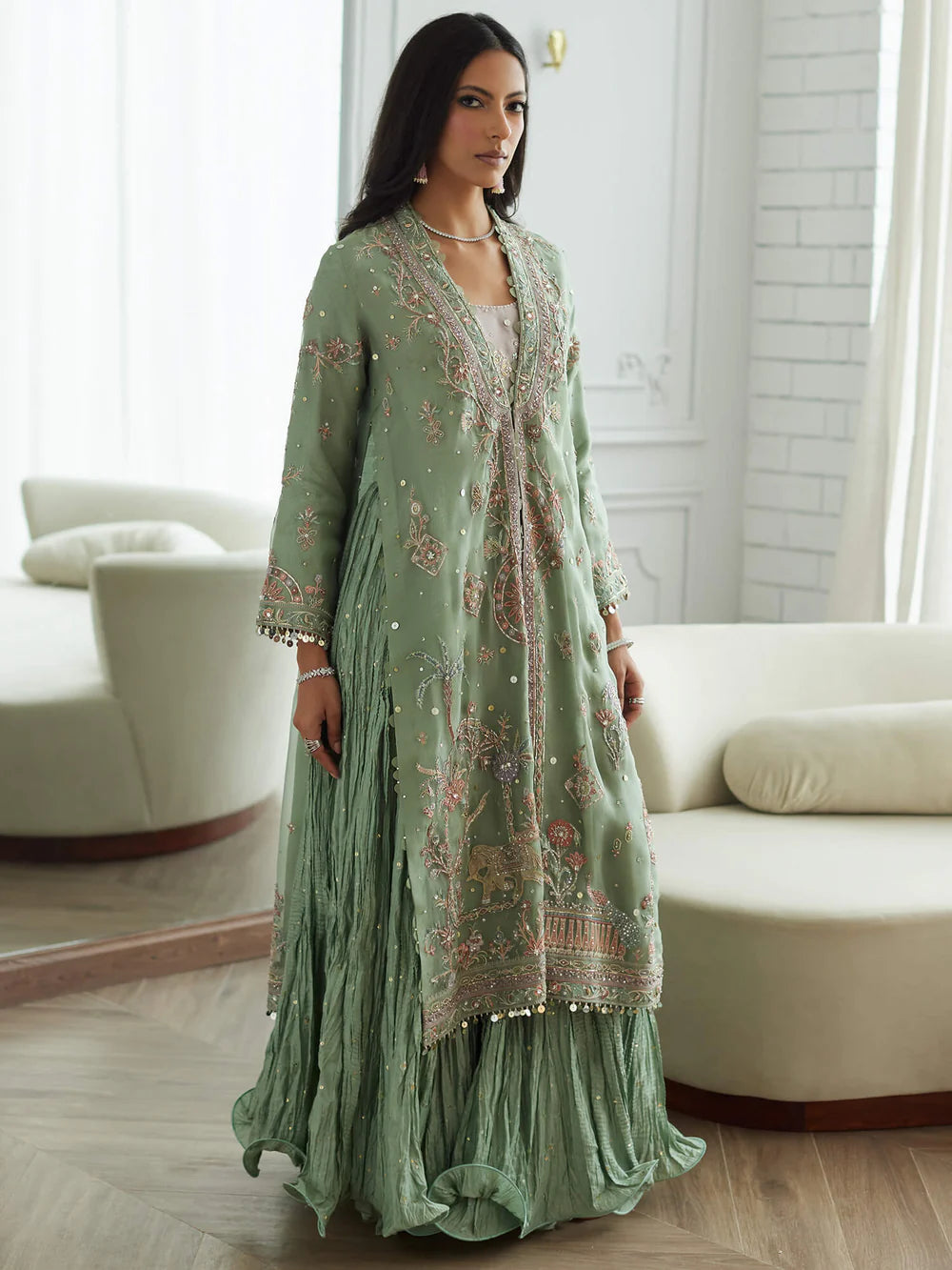 Woman wearing a green embroidered outfit in a room with white furniture.