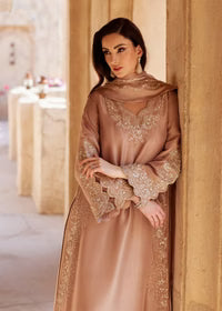 Woman in a beige embroidered dress standing against a beige wall.