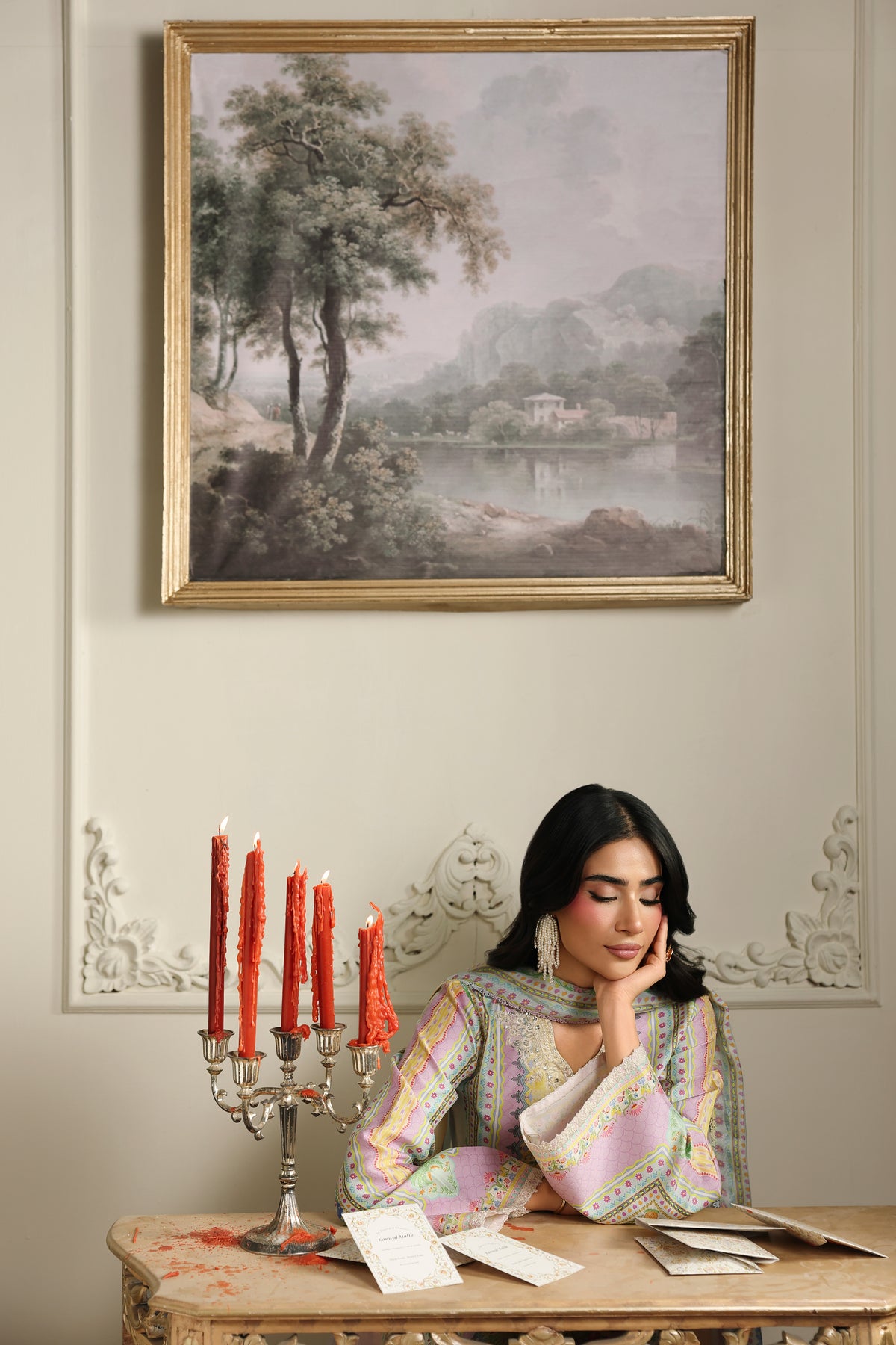 Woman sitting at a table with lit candles and a landscape painting on the wall.