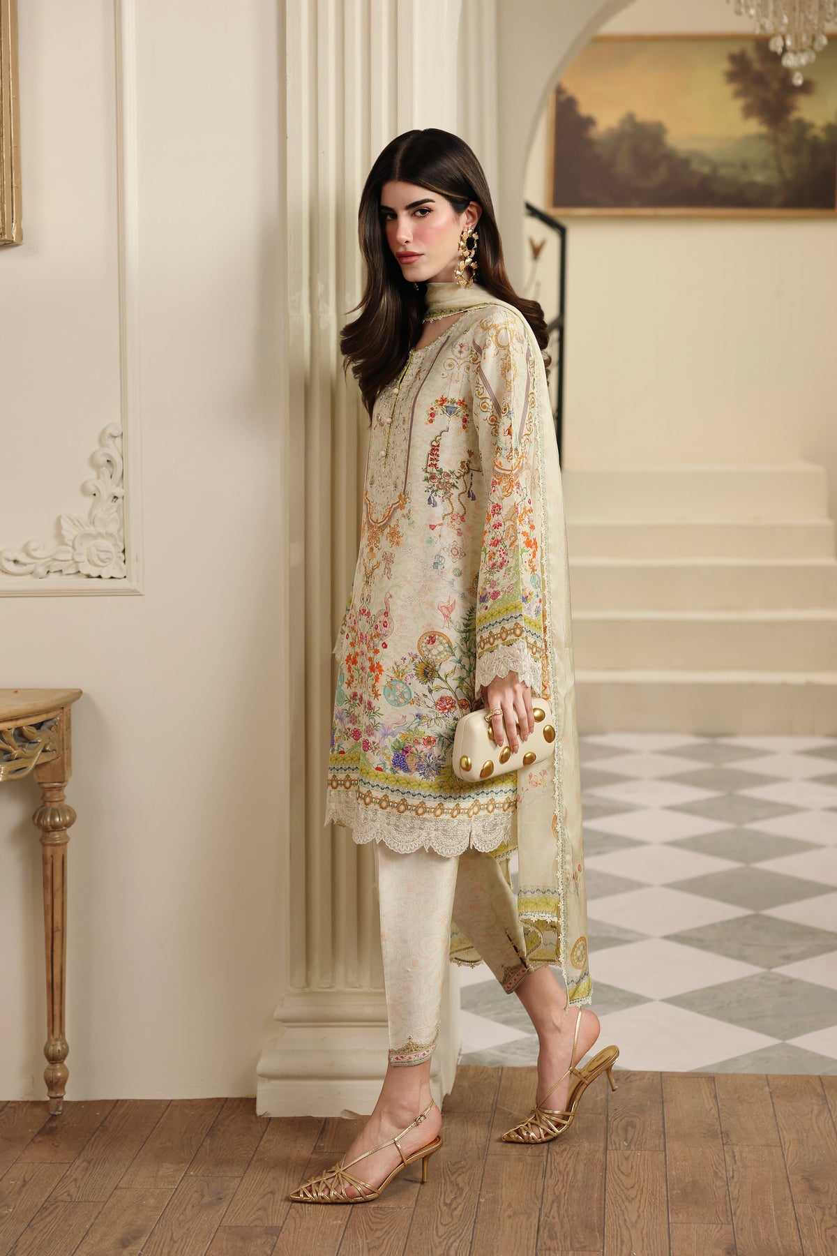 Woman in a floral embroidered outfit standing in an elegant interior setting.