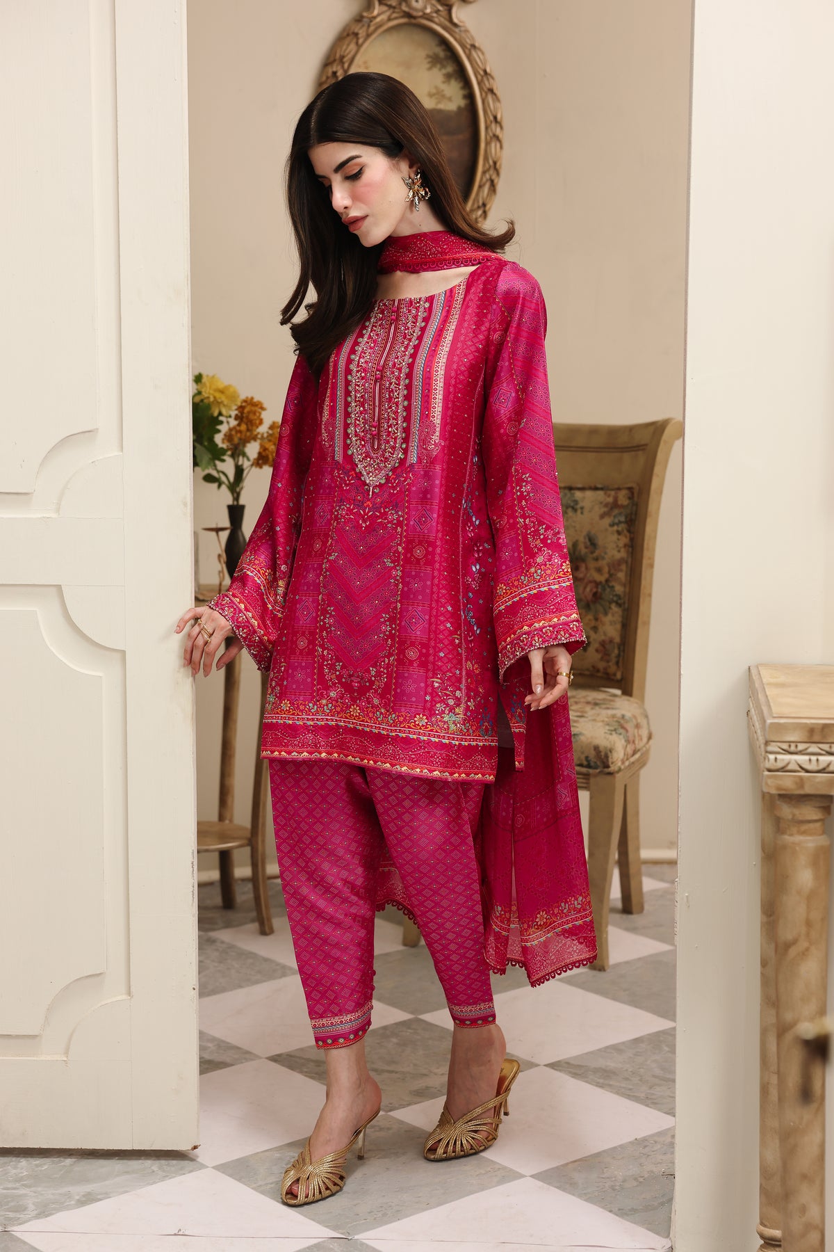 Woman in a pink embroidered traditional outfit standing in a decorated room.