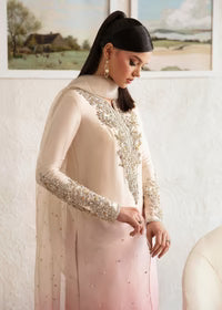 Woman wearing an ivory and blush pink embroidered ombre dress with a sheer dupatta in an elegant indoor setting.
