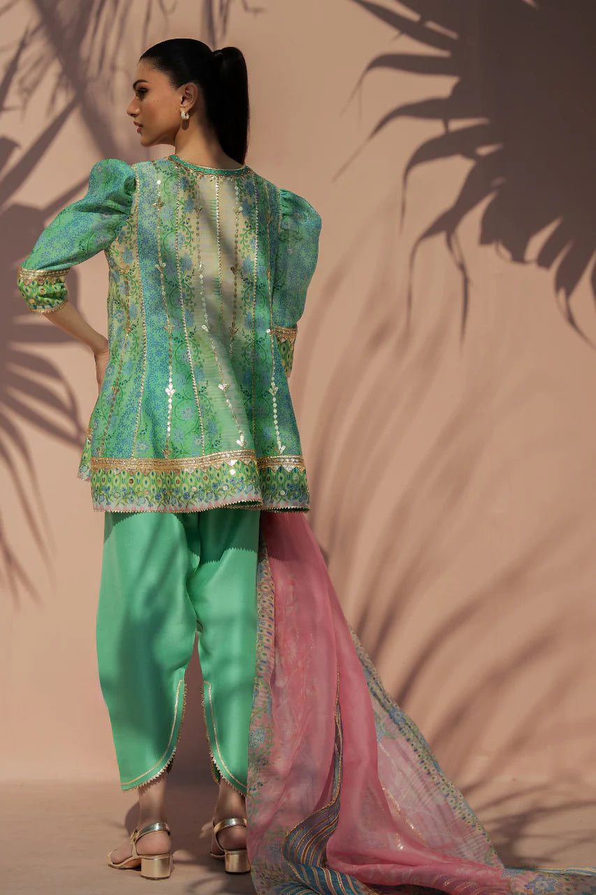 Woman in a green traditional outfit with a pink dupatta against a beige background