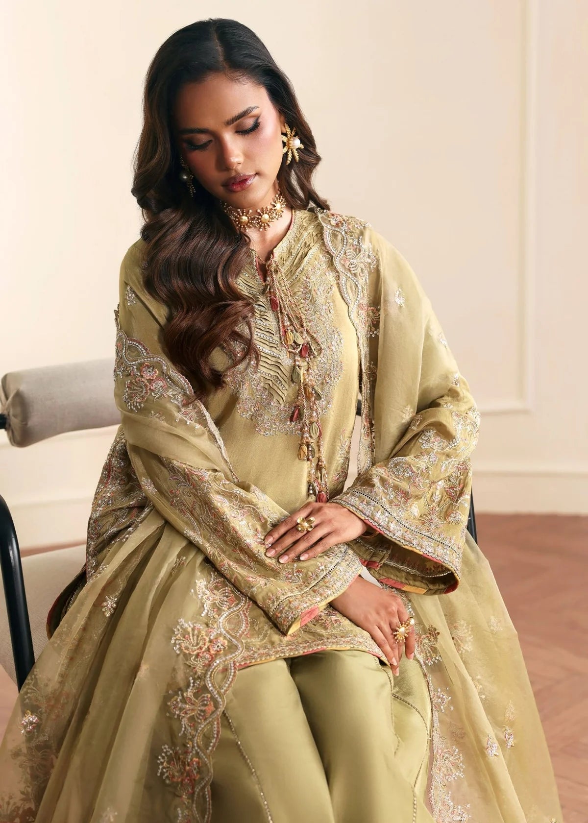 Woman in a light green traditional outfit with intricate patterns sitting on a chair.