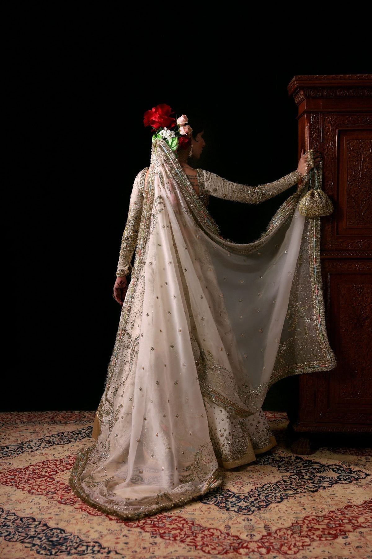 Woman in a traditional outfit with a headscarf, standing on a patterned rug.