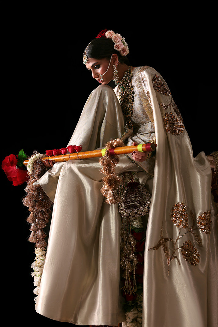 Woman in traditional attire holding a decorative staff against a black background