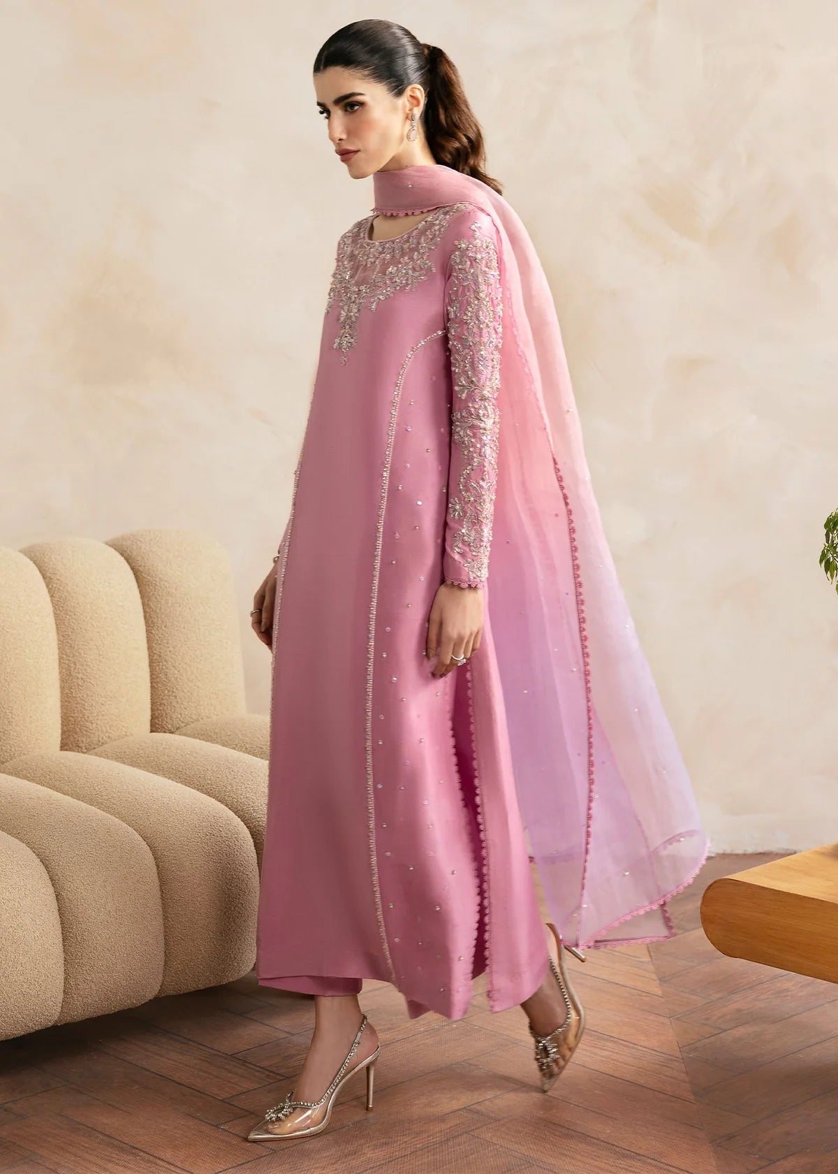 Woman wearing a pink traditional outfit with intricate designs in a room.