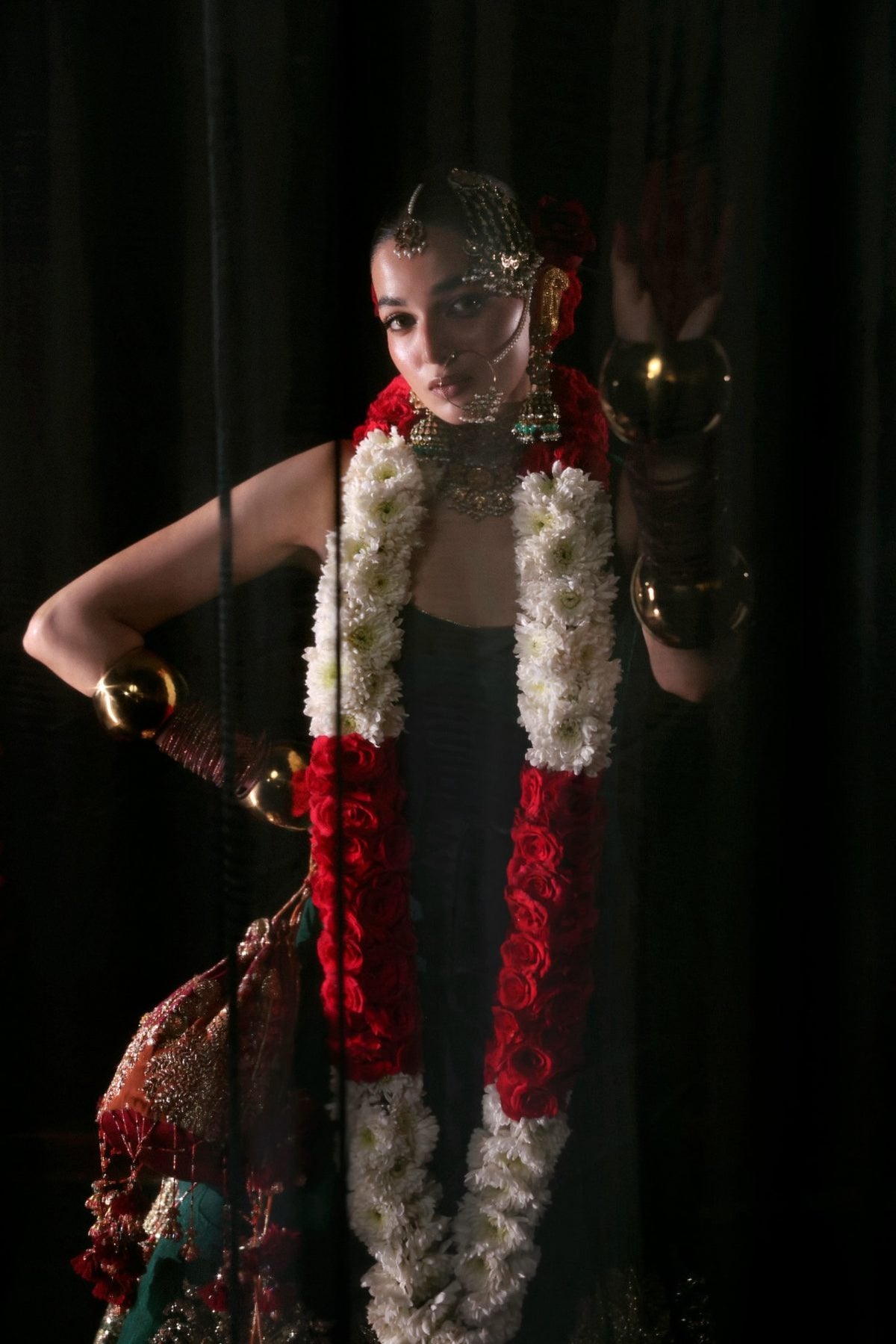 Person in traditional attire with red and white floral decorations against a dark background