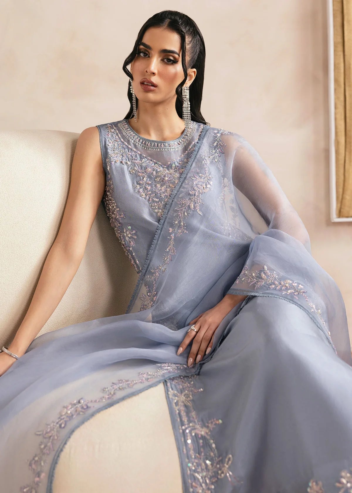 Woman wearing a light blue saree with intricate designs, sitting on a beige couch.