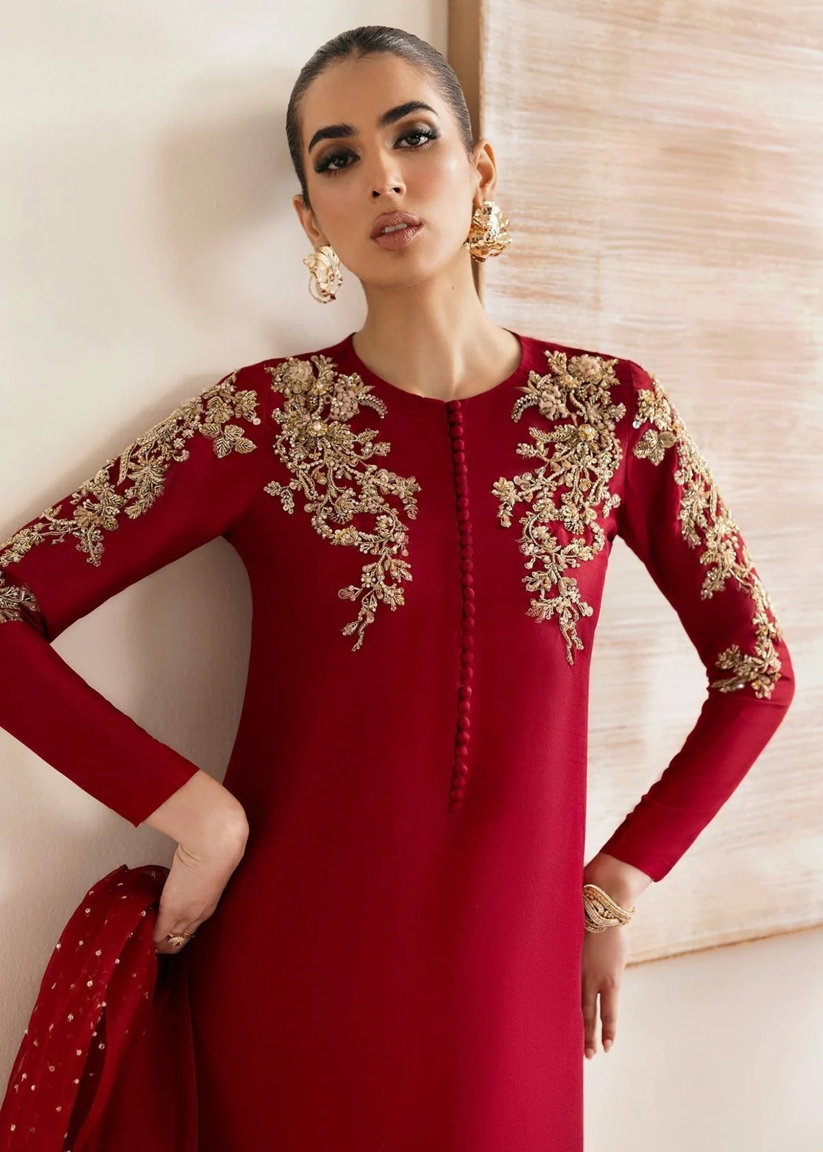 Woman wearing a red dress with gold embroidery against a neutral background