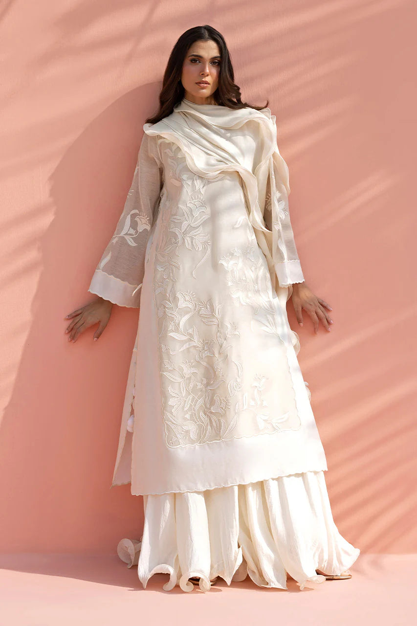 Woman wearing a white embroidered outfit with a matching shawl against a pink background