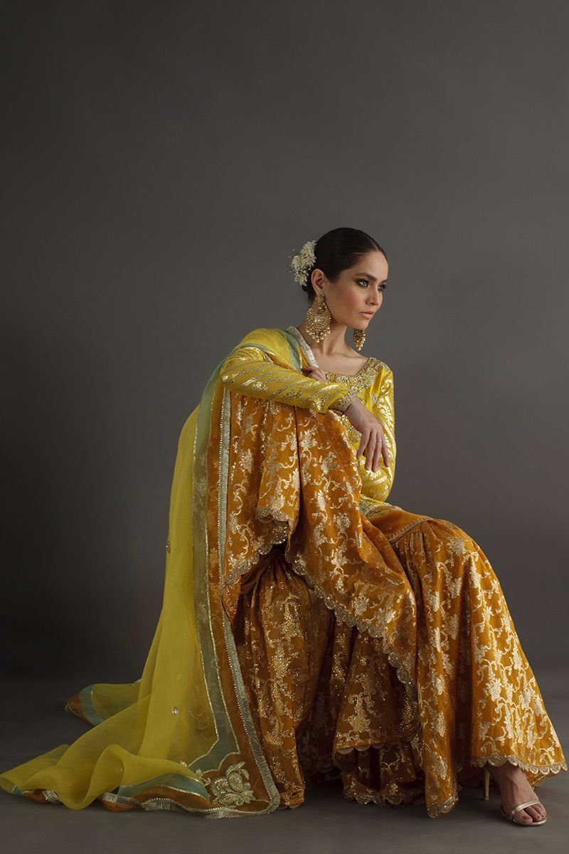 Woman in a yellow and brown saree sitting against a gray background