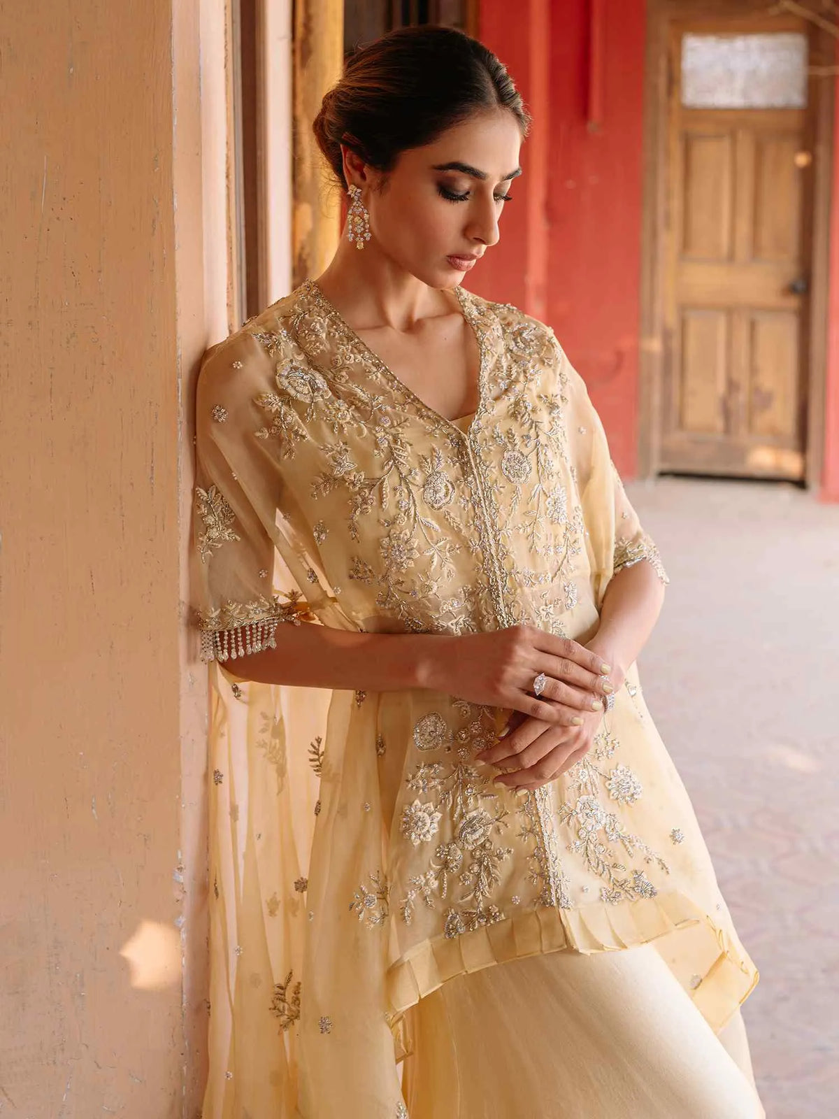 Woman in a light yellow embroidered traditional outfit standing indoors.