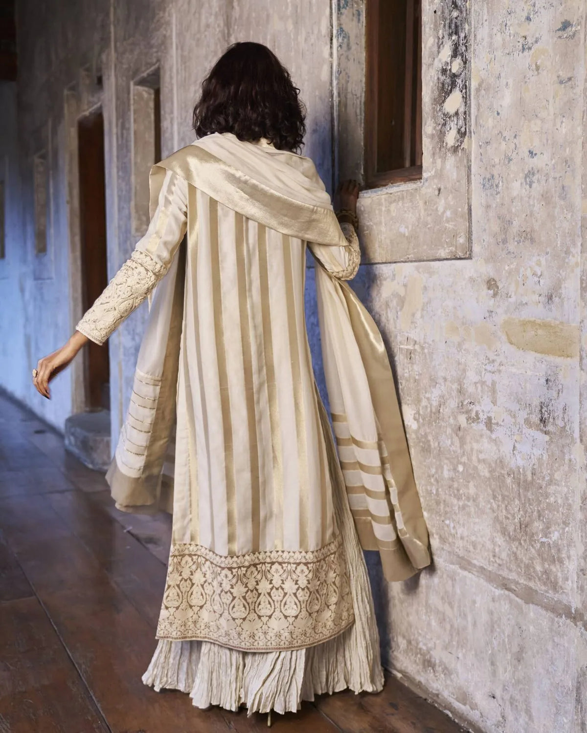 Woman in a traditional outfit standing in a dimly lit room with stone walls
