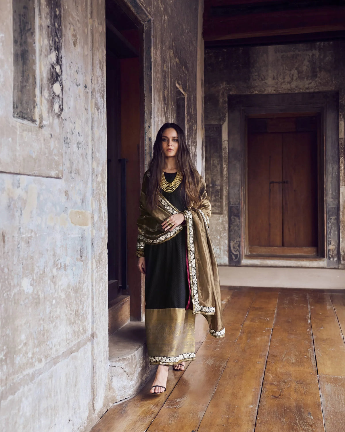Woman in traditional attire standing in a stone-walled room with wooden floor