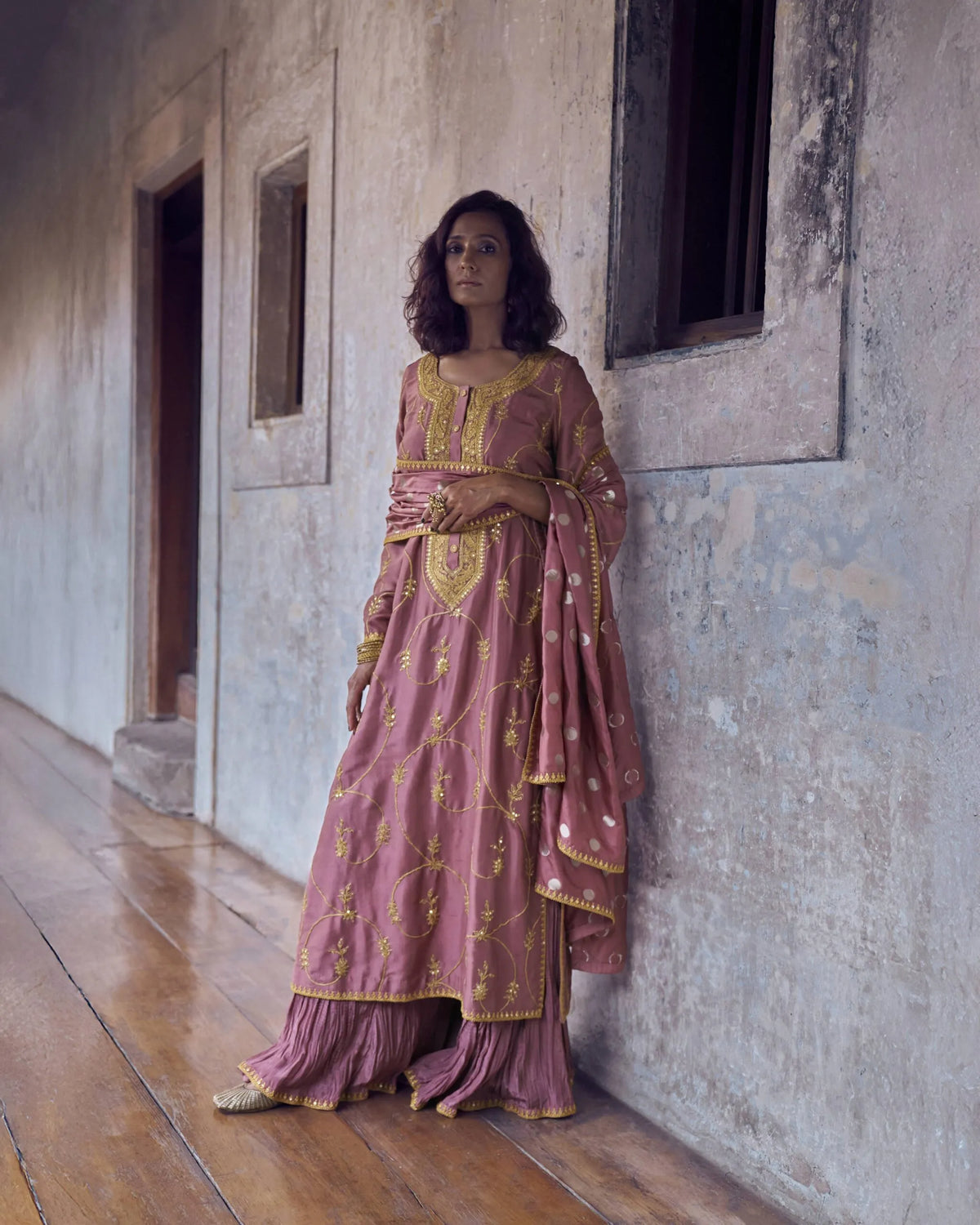 Woman wearing a dusty rose traditional outfit with intricate gold embroidery and a matching embellished dupatta.