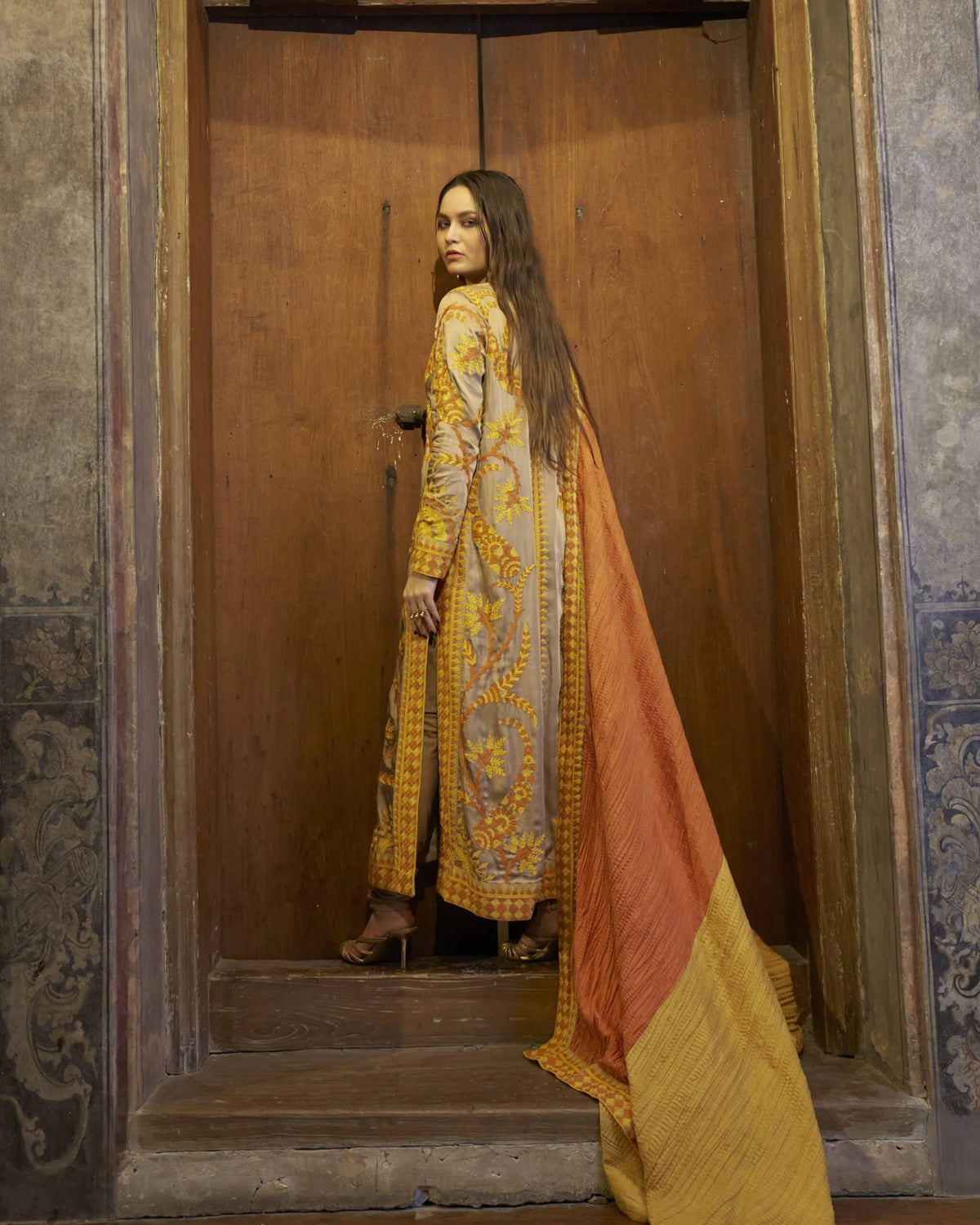 Woman in a traditional outfit standing in a doorway with ornate walls.