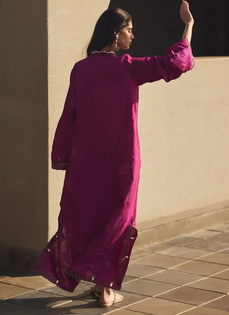 Woman in a long magenta dress standing against a beige wall.