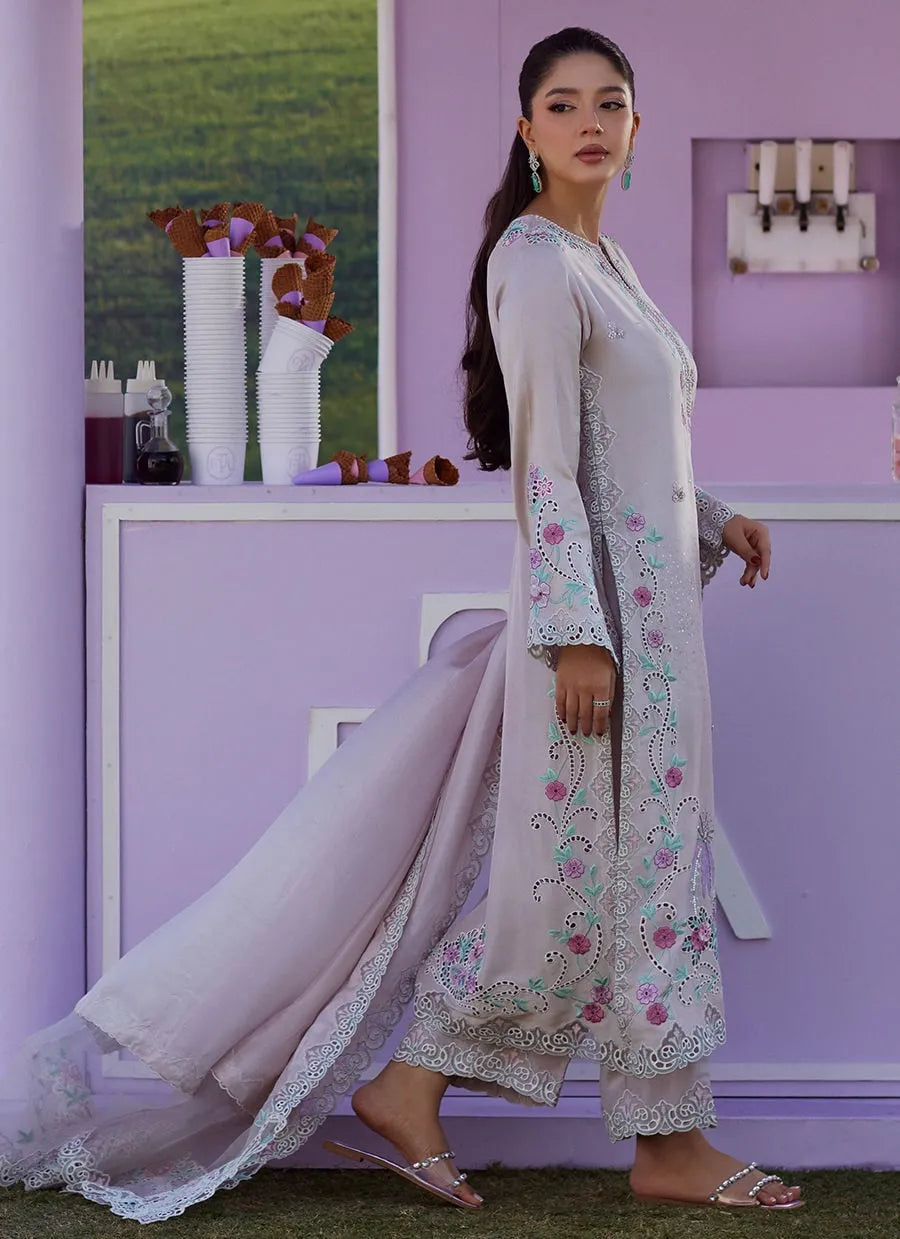 Woman in a floral outfit standing in front of a purple wall with decorative items.