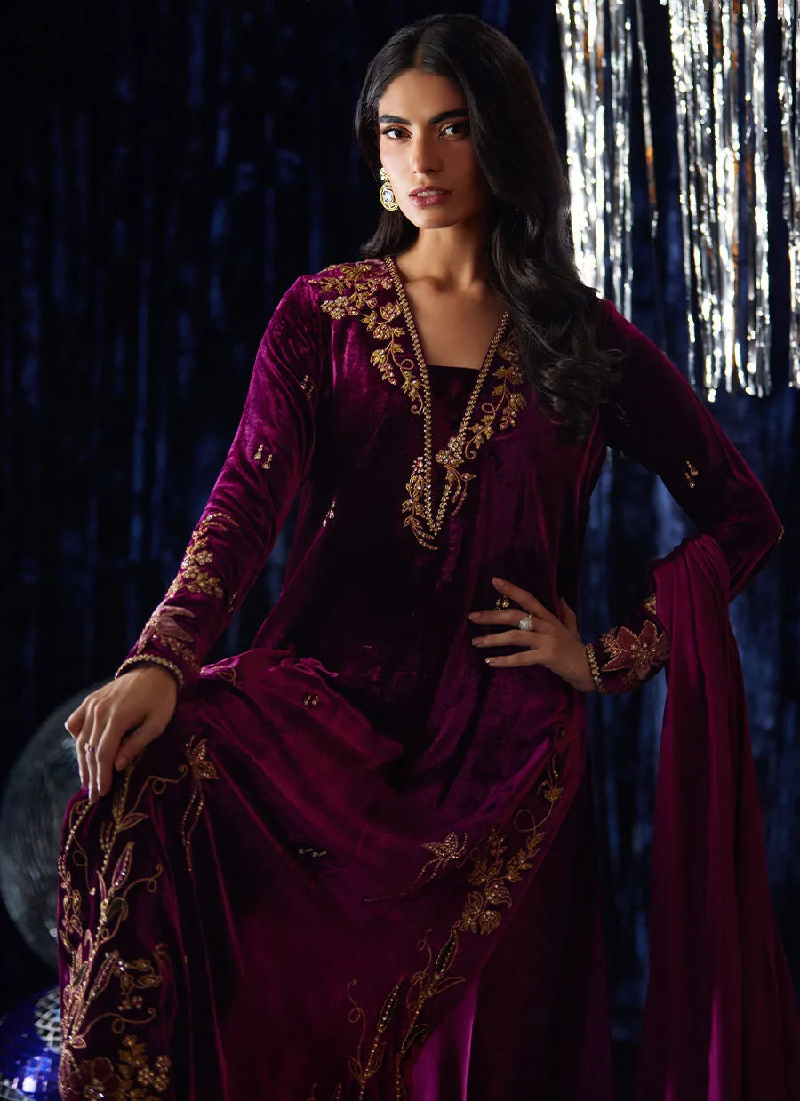 Woman in a purple traditional outfit with gold embroidery against a dark background
