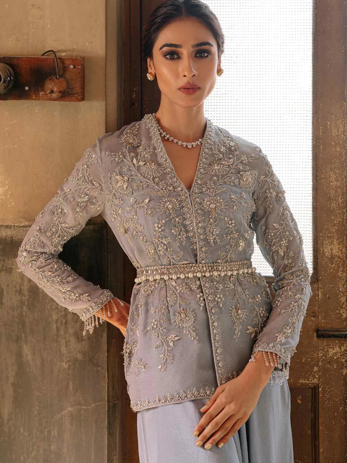 Woman wearing a light gray embroidered traditional outfit indoors.